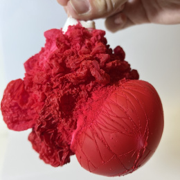 a hand holds a bunched up white balloon covered in fluffy-looking red clusters
