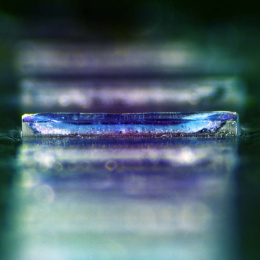 An iridescent column of bluish polymer layers. The third layer is in focus; the others are fuzzy.